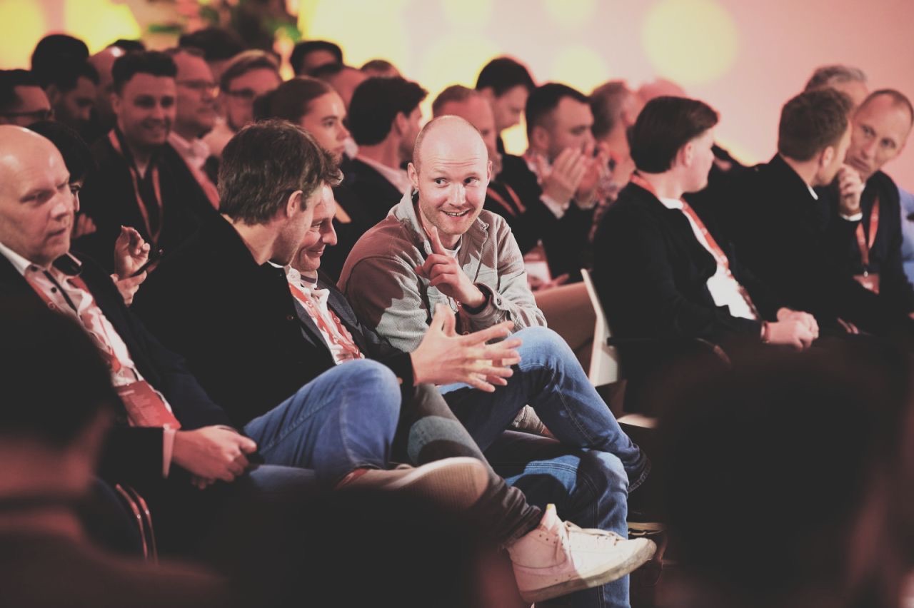 Congreszaal met publiek; Camiel Wits zit lachend op de eerste rij